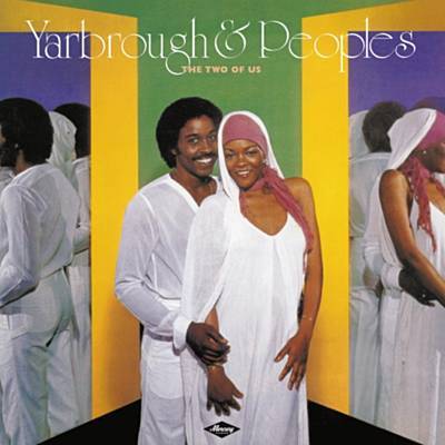 Pochette de l'album "The Two of Us" de Yarbrough & Peoples. Un homme et une femme se tiennent côte à côte, souriant, tous deux vêtus de blanc. La femme porte une capuche blanche et une coiffe rose. L'arrière-plan présente des miroirs reflétant leurs images, capturant l'essence de cette ambiance radio-funk classique.